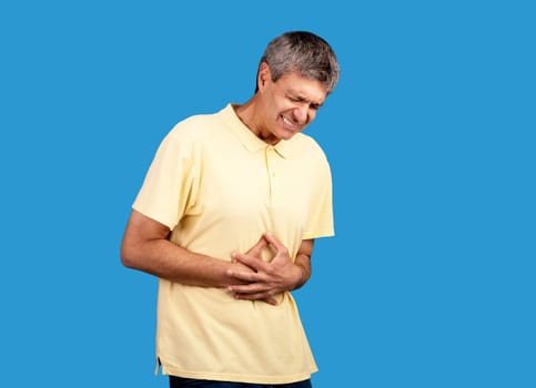 Mature man suffering from stomachache touching stomach on blue background