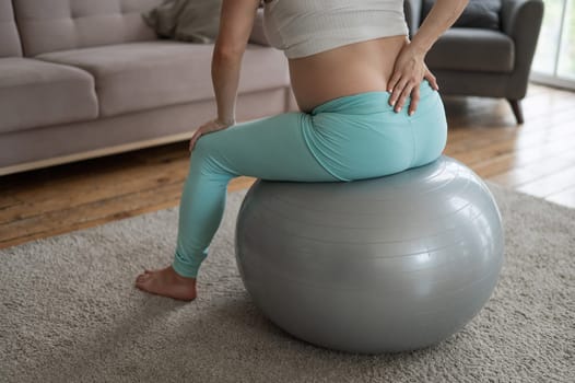 Caucasian pregnant woman suffers from back pain. Fitball training during pregnancy.