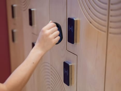 A woman opens the electronic lock of a cubicle in a locker room with a bracelet.