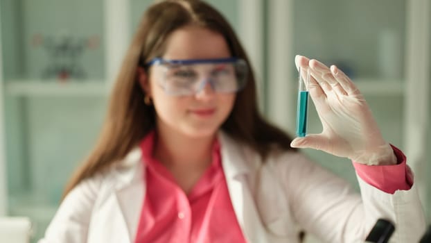 Scientist student woman looks at blue solution and test tube working in equipped laboratory