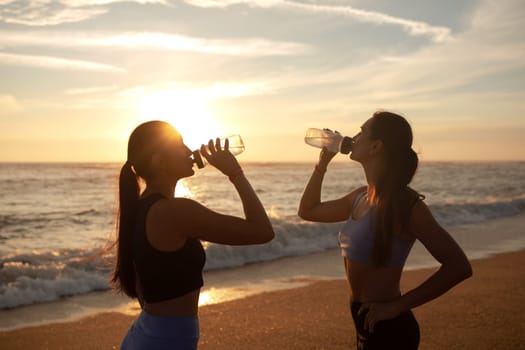 Tired millennial caucasian twins sisters women drinking bottle of water after jogging, enjoy break from fitness