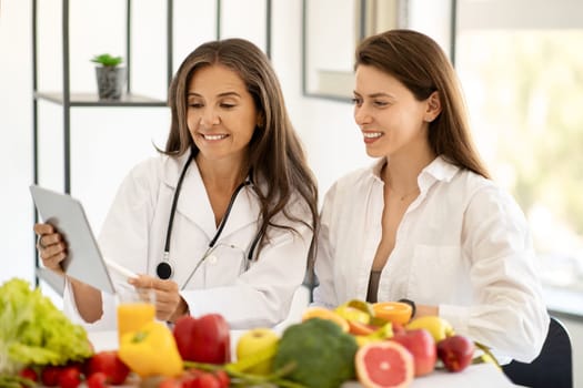 Happy mature caucasian doctor nutritionist in white coat consultation young woman