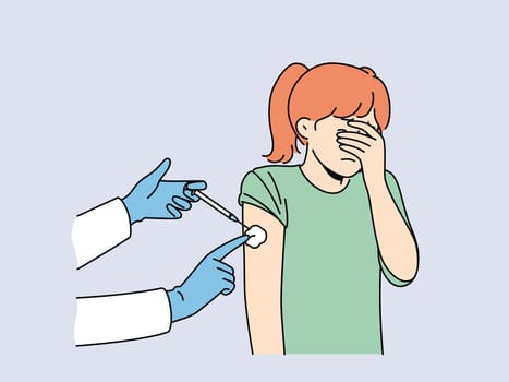Crying little girl is afraid of injections and closes eyes during injection in shoulder