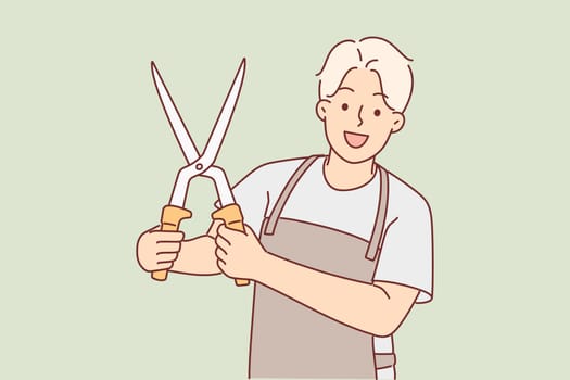 Man with garden shears in working apron demonstrates tool for trimming branches of bushes and trees