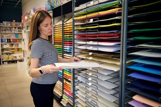 Confident woman choosing color paper in stationery shop. Saleswoman works on merchandising in school stationery store