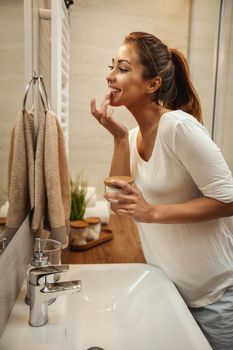 Shot of an attractive young woman applying facial moisturizing cream in the bathroom at home.