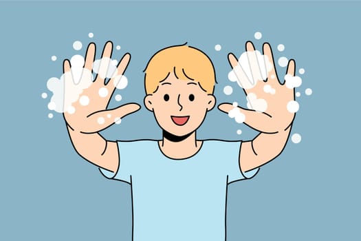 Little boy with foam shows soapy palms, recommending washing hands and following hygiene rules
