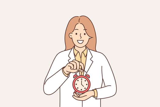 Woman doctor holding alarm clock recommending sticking to schedule for taking medications