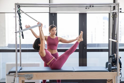 Asian woman doing pilates with trainer on cadillac reformer.