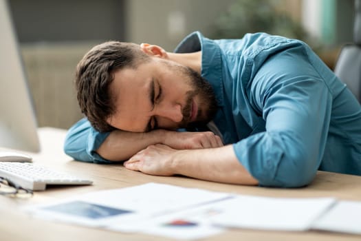 Overwork Concept. Exhausted male employee sleeping at desk with papers in office