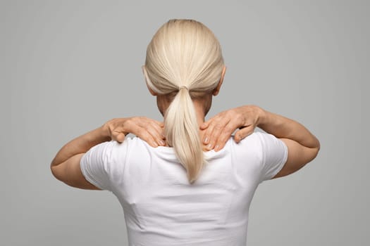 Unrecognizable blonde woman self massaging her shoulders, rear view