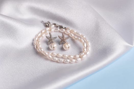 Elegance pearl bracelet and earring on silk fabric background. Jewellery and handmade accessories concept