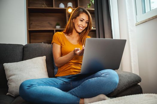 Shot of an attractive young woman sitting cross legged on the sofa and using her laptop to make a video call with someone at home.