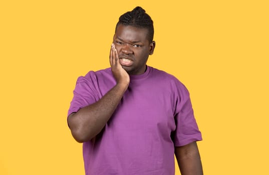 Unhappy black man suffering from tooth ache on yellow background