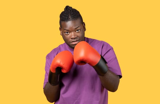 Confident young black boxer man wearing boxing gloves, yellow background