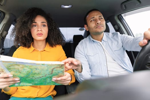 Perplexed Arab couple riding car holding and pointing at map