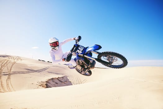 Sand, motor sports and man in air with motorbike for adrenaline, adventure and freedom in desert. Action, extreme sport and male person on bike on dunes for training, exercise and race or challenge