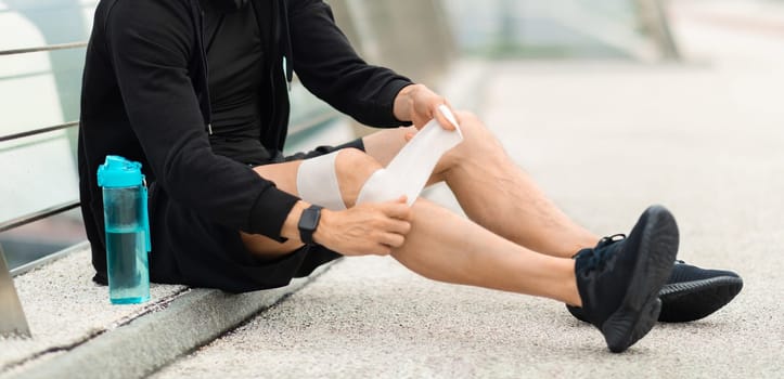 Sportsman suffering with knee pain during workout, putting bandage