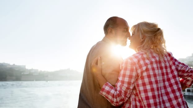Mature Love Story. Romantic Senior Couple Kissing Outdoors At Sunset Time, Silhouettes Of Loving Elderly Spouses Bonding Together During Walk Near Sea, Enjoying Their Marriage And Retirement Time