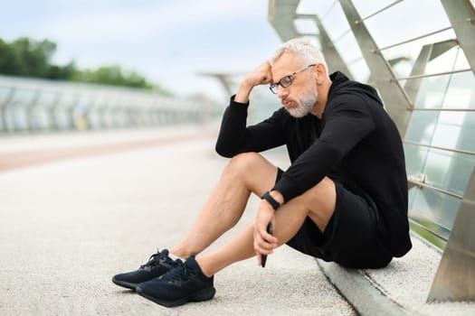 Exhausted elderly sportsman sitting on ground, working out outdoor