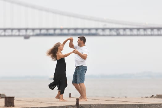 A romantic married couple dancing on the pier with a bridge on the background