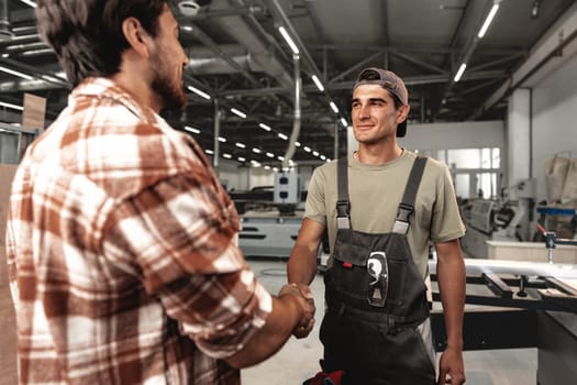 Two men shaking hands on background of workshop