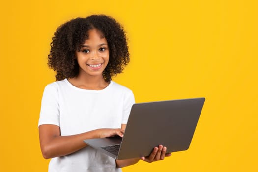Positive teenage black pupil girl in white t-shirt uses laptop, wach video lesson