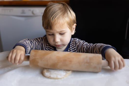 Family cooking - a little boy rolls out dough with a rolling pin