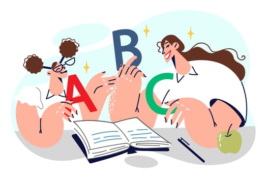 Schoolgirl learns alphabet together with elementary school teacher, sitting in classroom