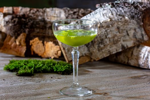 Glass of fresh green cold appetizing cocktail with froth decorated with straw and mint served on black counter