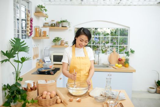 female mixing flour with eggs while using whisk. She is cooking bakery in domestic atmosphere