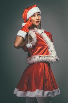 Woman in Santa Claus costume standing, looking at camera and thinking