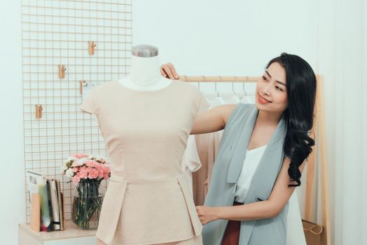 An Asian girl  is working in the workshop studio. She makes fitting on the dress on the mannequin.