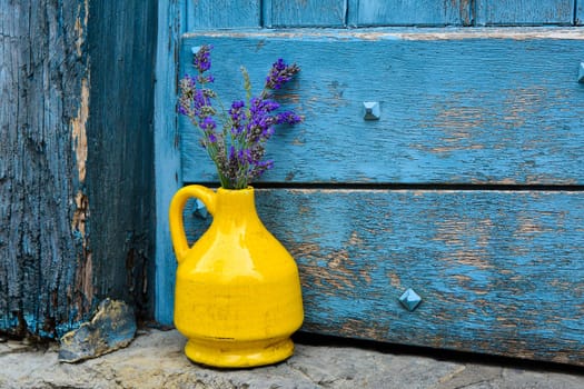 Lavender in a yellow vase on a background of blue shabby door