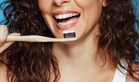 Laughing young european curly woman brushing teeth with toothpaste and toothbrush