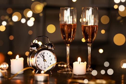 Watch, two glasses with champagne, candles against background of lights