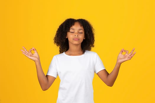 Calm adolescent african american girl in white t-shirt, meditates, enjoys silence