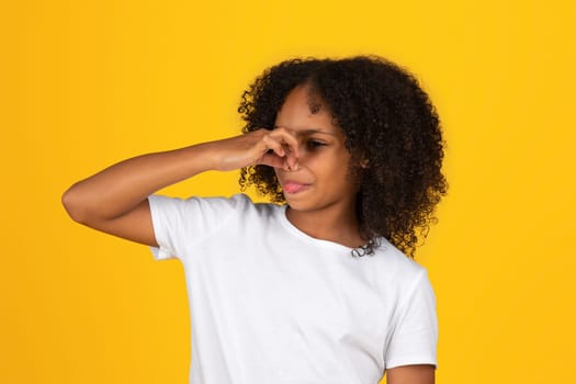 Sad adolescent african american girl in white t-shirt covering nose, suffering from bad smell