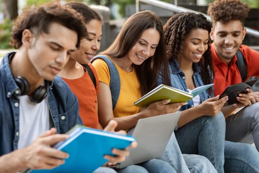 Group Of Young Multiethnic People Study Together Outdoors, Five Students Reading Books And Using Digital Tablet While Sitting Outside, Preparing For Exams Or Getting Ready For Classes, Closeup