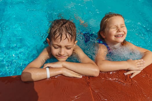Two happy kids having fun in the pool. Little brother and sister with pleasure spending time together in summer camp.