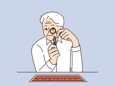Elderly man jeweler examines diamond through magnifying glass checking gems for authenticity