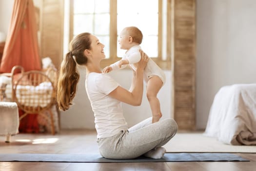 Happy young mother exercising with toddler kid at home