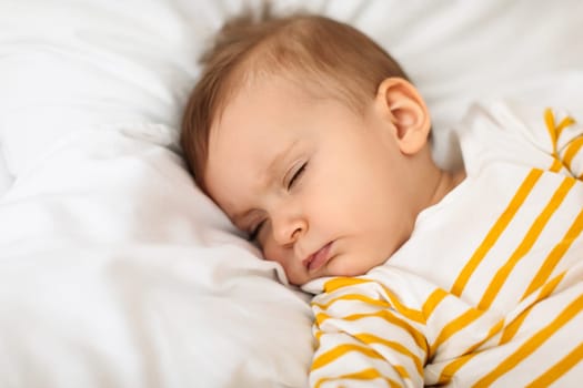 Little baby girl sleeping peacefully on bed and grimacing, resting during daytime sleep with eyes closed, copy space