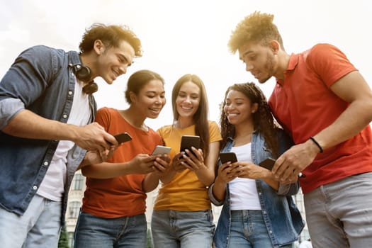 Group Of Young Multiethnic People With Smartphones In Hands Standing Outdoors, Happy Students Looking At Mobile Phone Screen With Interest, Checking New Educational App Or Website, Closeup Shot