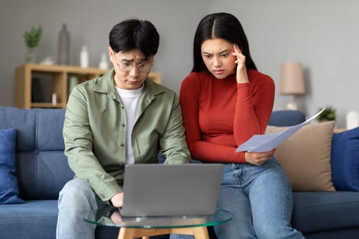 Depressed Asian Couple Looking At Laptop Doing Paperwork Indoors