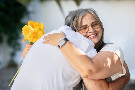 Happy old european husband and wife hugging with bouquet of flowers, celebrating anniversary