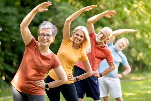 Group of sporty mature people doing stretching exercises at park, happy senior men and women training outdoors, smiling elderly friends exercising outside, enjoying active lifestyle on retirement