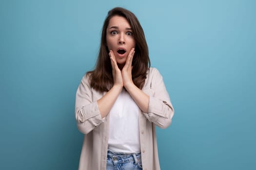 surprised upset brunette young female adult in a shirt and jeans on a background with copy space