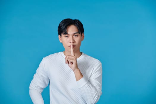 Portrait of serious young Asian man showing a sign of silence gesture putting fingers in mouth