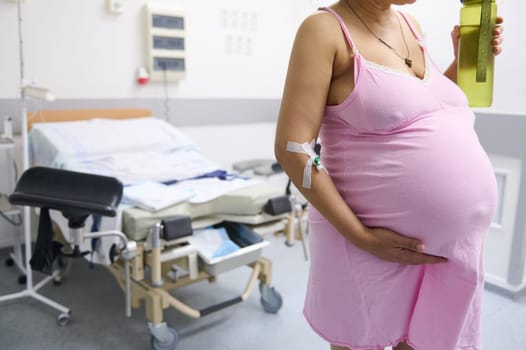 Pregnant woman, birthing mother in delivery room, holding hands on belly, drinking water between contractions. Close-up.